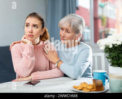 Ältere Frau beruhigt geächtete Erwachsene Tochter am Tisch Stockfoto