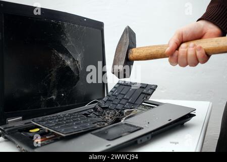 Der Mann hat den Laptop mit einem Hammer zerstört. Nervöse Arbeit, Buggy Computer, Fehler, langsames Internet, nicht im Spiel gespeichert, gedruckter Text, hängt. Schlechter alter Computer Stockfoto