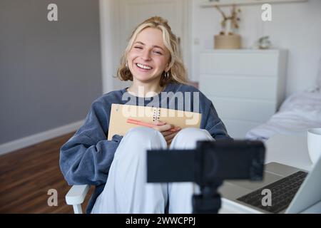 Porträt einer lächelnden, charismatischen jungen Frau, Inhaltsersteller, nimmt Videos auf der Digitalkamera auf, lacht und sieht glücklich aus, benutzt Tagebuch, schreibt hinein Stockfoto