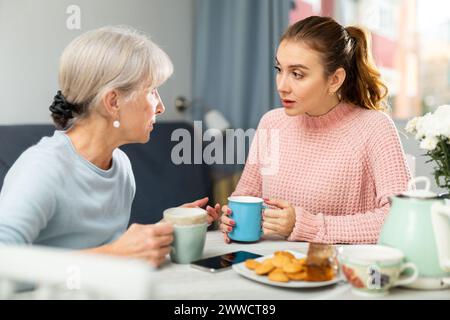 Seniormutter und Erwachsene Enkelin, die sich unterhalten und Tee trinken Stockfoto
