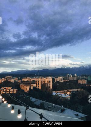 Eine atemberaubende Stadtlandschaft mit Bergen im Hintergrund, umgeben von grünen Bäumen unter einem blauen Himmel mit weißen Wolken. Stockfoto