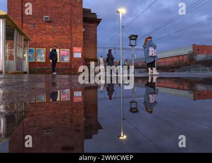 Bahnhof Edge Hill, Passagiere, die auf einen Zug der Northern Rail warten, spiegeln sich in einer Pfütze auf dem Bahnsteig Stockfoto