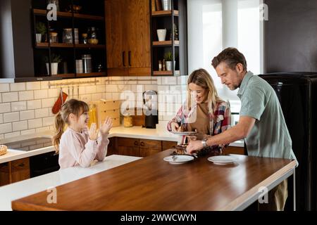 Eine herzerwärmende Szene entfaltet sich, während eine Familie einen köstlichen Schokoladenkuchen zusammen in der Wärme ihrer sonnendurchfluteten Küche genießt und Lächeln und cr teilt Stockfoto