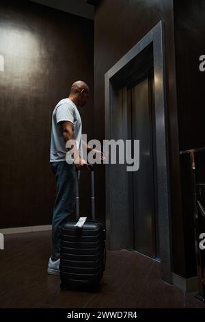 afroamerikanischer Mann mit Koffer, der den Knopf des Fahrstuhls in der Hotelhalle drückt Stockfoto