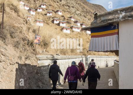 Pilger passieren kleine Meditationshütten, während sie Umgehungen (kora) rund um das Kloster Labrang machen. Xiahe County, Provinz Gansu, China. Stockfoto