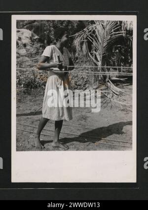 Beschreibung: Seilherstellung aus „Kokos“, gewonnen durch verrottete Kokosfasern. Das Bild zeigt eine Frau, die drei Stränge zu einem vereint. Ort: Seychellen Datum: 1950-1959 Stockfoto