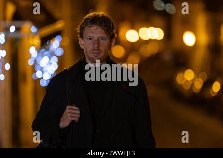 Ein Mann mit schwarzem Mantel und schwarzem Schal läuft nachts die Straße entlang Stockfoto