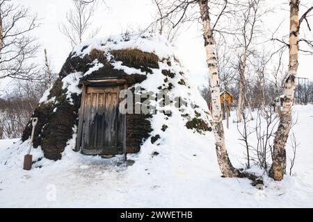 Malerisches Bild einer mit Moos und Schnee bedeckten Holzhütte in einem Saami-Lager in der Nähe von Abisko in Nordschweden. Stockfoto