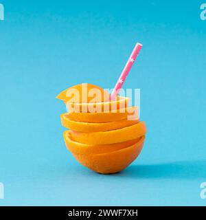 Sommerkomposition mit frisch gestapelten Orangenscheiben und rosafarbenem Stroh auf hellblauem Hintergrund. Kreatives Konzept für gesunde Ernährung. Stockfoto