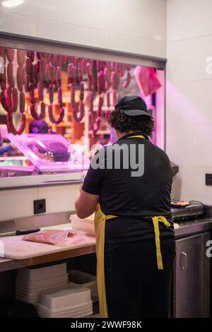 Vertikales Porträt eines Metzgers, der in seiner Metzgerei frisch geschnittenes Fleisch verpackt. Die Szene fängt das Wesen des traditionellen Fleischs vor ein Stockfoto