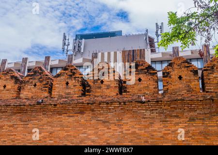 Backsteinmauer im antiken Stil mit modernen Strukturen und Handytürmen dahinter in Chiang Mai, Thailand Stockfoto