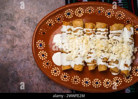 Gebratene Kartoffeltacos mit Sahne und Käse in einem mexikanischen Schlammgericht. Tacos dorados, mexikanisches Essen. Stockfoto