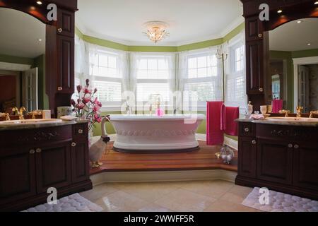 Hauptschlafzimmer en Suite mit freistehender weißer Badewanne auf erhöhter Plattform und seine und ihre Waschtische im eleganten Stil Haus, Quebec, Kanada Stockfoto