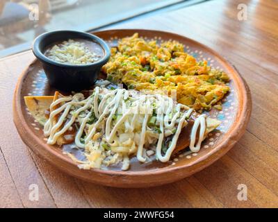 Traditionelles mexikanisches Frühstück mit „Huevos a la mexicana“, Chilaquiles mit Sahnedrizzle und Bohnen mit Käse, serviert auf einem Ru Stockfoto