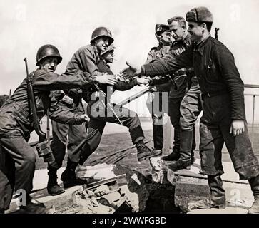 Torgau, Deutschland, 25. April 1945 amerikanische Truppen (links) greifen auf einer zerstörten Brücke über die Elbe nach der historischen Verbindung in Torgau die Hände von Soldaten der sowjetischen Armee. Stockfoto