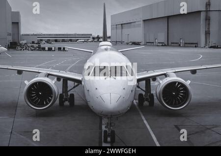 Vorderansicht eines modernen Zweibettflugzeugs, das auf dem BetonAsphalt mit Fahrbahnmarkierungen in einem großen Flughafen sitzt. Schwarz-weiß Stockfoto