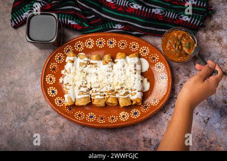 Frau löffelt Salsa auf einem Teller mit goldenen Kartoffeltacos. Mexikanisches Essen. Stockfoto