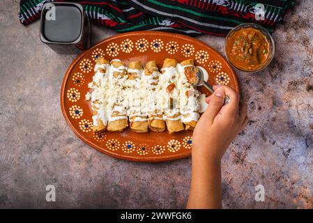 Frau löffelt Salsa auf einem Teller mit goldenen Kartoffeltacos. Mexikanisches Essen. Stockfoto