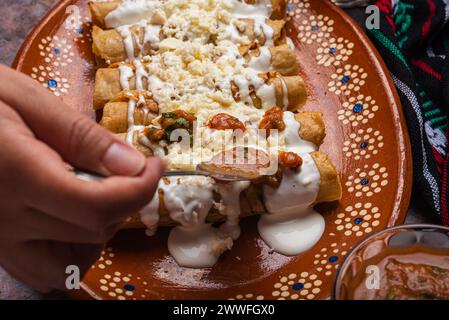 Frau löffelt Salsa auf einem Teller mit goldenen Kartoffeltacos. Mexikanisches Essen. Stockfoto