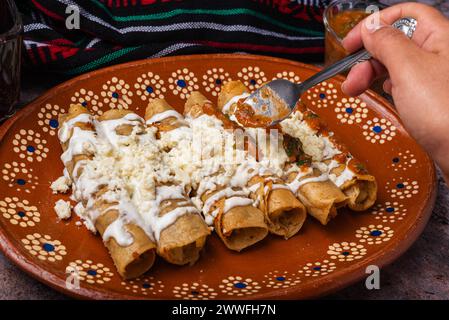 Frau löffelt Salsa auf einem Teller mit goldenen Kartoffeltacos. Mexikanisches Essen. Stockfoto