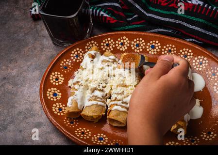 Frau löffelt Salsa auf einem Teller mit goldenen Kartoffeltacos. Mexikanisches Essen. Stockfoto