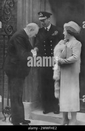 Ein Foto zeigt, wie König George VI. Und Königin Elisabeth I. von Winston Churchill in der Downing Street 10 begrüßt werden. Dieses Bild wurde um 1940 aufgenommen und zeigt einen bedeutenden Moment der Einheit zwischen den britischen Führern während des Zweiten Weltkriegs. Es zeigt die enge Zusammenarbeit zwischen der Monarchie und der Regierung bei der Führung der Nation durch eine der dunkelsten Zeiten. Stockfoto