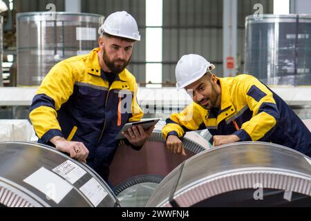 Zwei Fabrikarbeiter untersuchen einen Stapel großer Stahlspulen in einer industriellen Umgebung oder in einer Produktionsanlage. Stockfoto