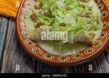 Grüne Enchiladas mit Salat serviert in einer Tonschale auf einem Holztisch. Stockfoto