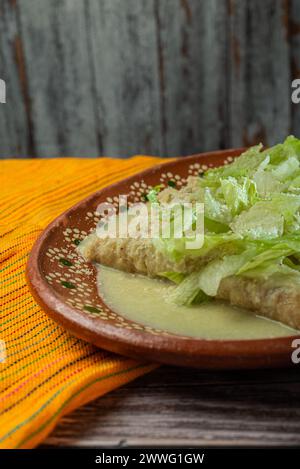 Grüne Enchiladas mit Salat serviert in einer Tonschale auf einem Holztisch. Stockfoto