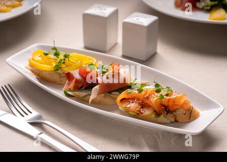 Teller mit gemischter italienischer Vorspeise Bruschetta mit gehacktem Lachs, Marmelade und Pfeffer auf Ciabatta-Brot, garniert mit Tomaten und Mikrogrün Stockfoto