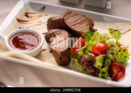 Gegrillte Würstchen oder Kupaty werden mit Gemüse, Salat und Ketchup auf einem weißen Teller serviert. Grillmenü Stockfoto