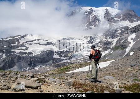 Man Hiking Skyline Trail im Mount Rainier National Park. Der Berg Rainier blickt durch die Wolken. Bundesstaat Washington. Stockfoto