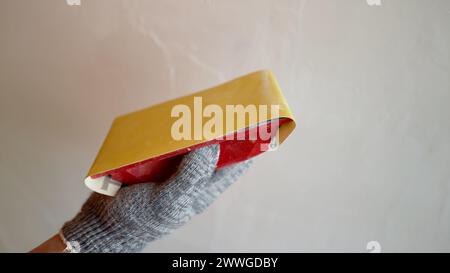 Der Gipser glättet die Wand mit Schleifpapier. Das Schleifen von Wänden nach dem Einbringen und Reparieren. Ablösen von unebenen Oberflächen an einer Kittwand, Schleifen des Stockfoto