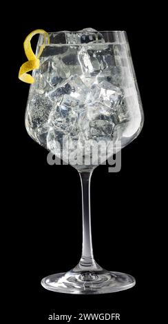 Elegantes Kristallglas von Gin Tonic garniert mit spiralförmiger Zitronenschale isoliert auf schwarzem Hintergrund. Stockfoto