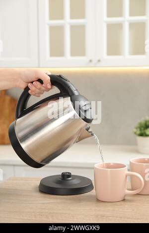 Frau, die heißes Wasser aus dem Wasserkocher in die Tasse in der Küche gießt, Nahaufnahme Stockfoto