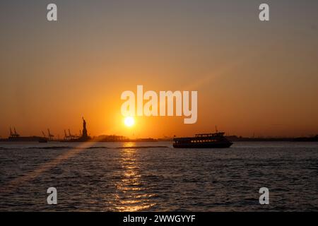 Die Sonne untergeht hinter der Freiheitsstatue und malt die Szene in warmen Tönen. Stockfoto