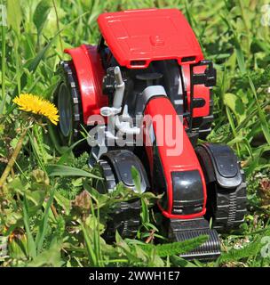 Roter Traktor im hohen grünen Gras im Frühjahr. Landwirtschaftliche Arbeiten im Frühjahr. Getreideanbau. Agrartraktor auf grünem Hintergrund Stockfoto
