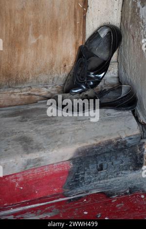 Ein Paar schmutzige, staubige, schwarze Lederschuhe, die auf einer Holztür vor einem Haus in Tiflis, Republik Georgien, platziert werden. Stockfoto