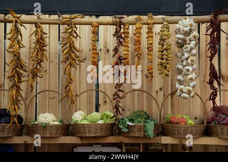 Hängende, getrocknete, rote und gelbe heiße Paprika, Knoblauch und Blumen und frisches Gemüse in Körben, attraktiv angeordnet auf einem Lebensmittelmarkt in Tiflis, Capi Stockfoto