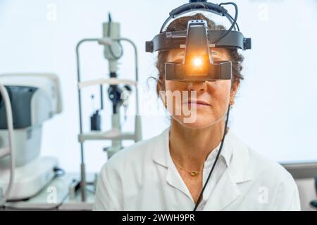 Portraitfrontalsicht einer Augenärztin mit dem Licht einer Stirnlampe eines Retinoskop Stockfoto