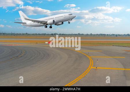 Blick auf die Kurve vom Rollweg auf die Start- und Landebahn und ein Passagierflugzeug, das vor dem Hintergrund abhebt. Stockfoto