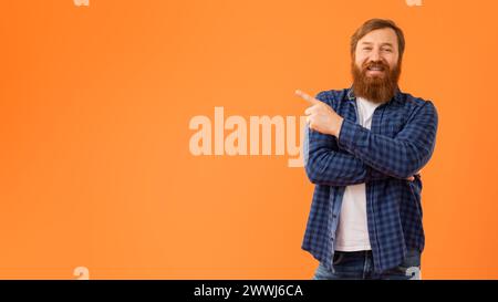 Rothaariger Mann mit stilvollem Bart posiert mit dem Finger zur Seite zeigend, Studio Stockfoto