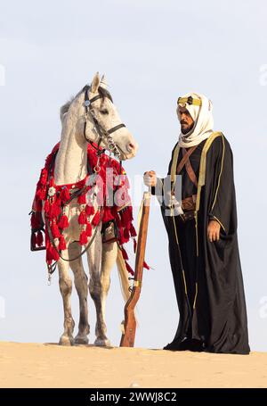 Saudischer Mann in traditioneller Kleidung mit seinem weißen Hengst Stockfoto
