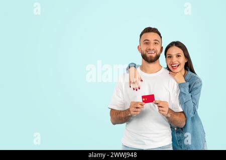 Glückliches europäisches Paar hält Kreditkarte vor blauem Hintergrund Stockfoto
