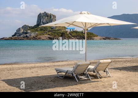 Sonnenliegen mit Sonnenschirm am Sandstrand von Agios Stefanos. Die griechische Insel Kos Stockfoto