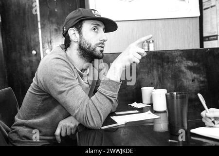 Junger Mann, der die Bronx trägt, New York City, USA. Yioung erwachsener Mann, der ein Gespräch in einem Café führt. MRYES New York City Roosevelt Ave, Queens New York Vereinigte Staaten von Amerika Copyright: XGuidoxKoppesx Stockfoto