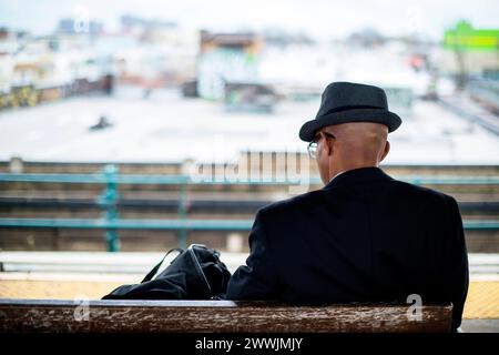 Afroamerikanische U-Bahn-Pendler New York City, USA. Afroamerikanischer Mann, mit Have und Mantel, sitzend auf einer U-Bahn-Station, während er auf seinen U-Bahn-Zug zum Flughafen JFK wartete. Unscharfer oder unscharfer Hintergrund. New York City Crescent Street Subway Station New York Vereinigte Staaten von Amerika Copyright: XGuidoxKoppesx Stockfoto