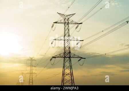 Eine Hochspannungsleitung steht hoch vor einer hellen Sonne im Hintergrund und veranschaulicht die Infrastruktur der Energieübertragung und -Verteilung. Stockfoto