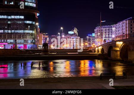 Beleuchtete Gebäude und Lichter in der Nähe eines Flusses bei Nacht in Skopje im Norden Mazedoniens Stockfoto