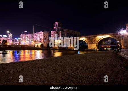 Beleuchtete Gebäude und Lichter in der Nähe eines Flusses bei Nacht in Skopje im Norden Mazedoniens Stockfoto